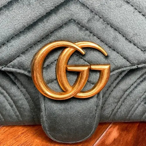 Green quilted handbag with gold double G logo on a wooden surface