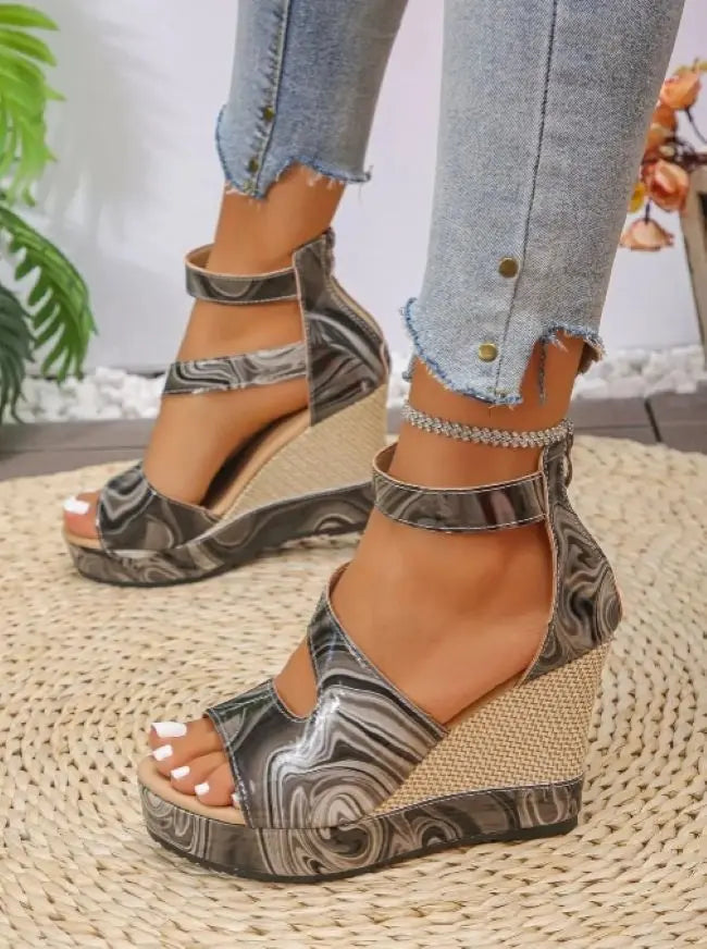 A person wearing wedges with a black and white marbled patterned design on a woven surface.