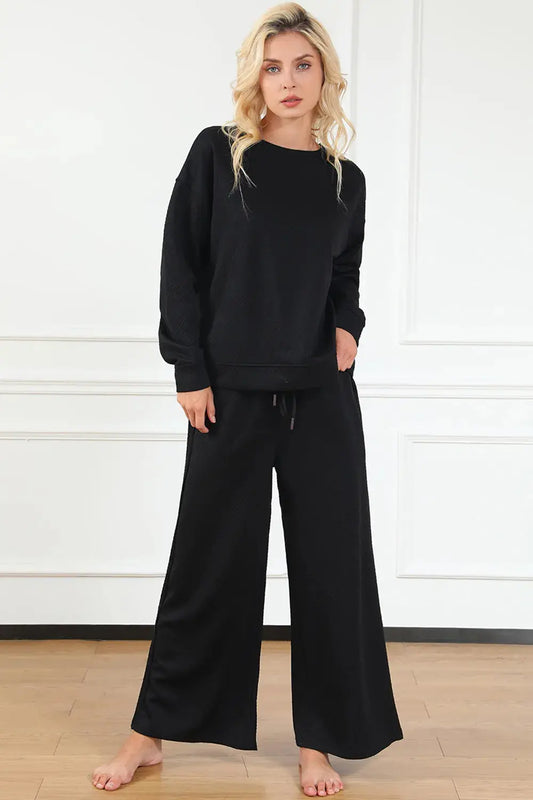 Woman wearing a black lounge set against a white wall.