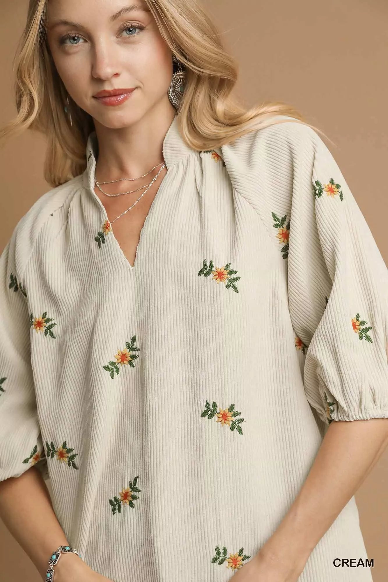 Woman wearing a cream-colored blouse with floral embroidery on a beige background