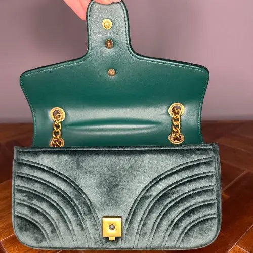 Green handbag with gold accents held open by a hand on a wooden surface.