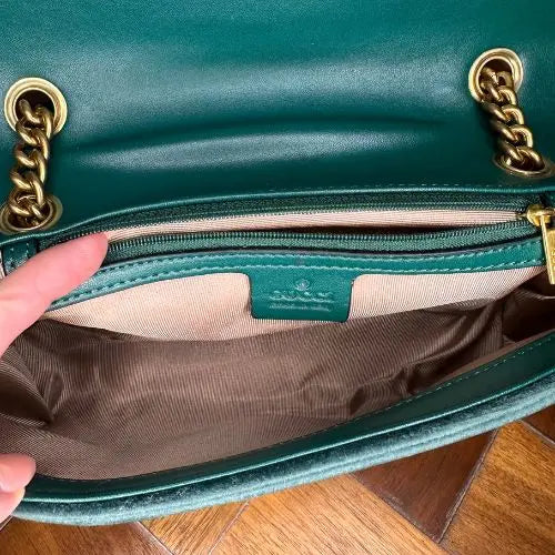 Green handbag with gold chain detail, open to show interior.
