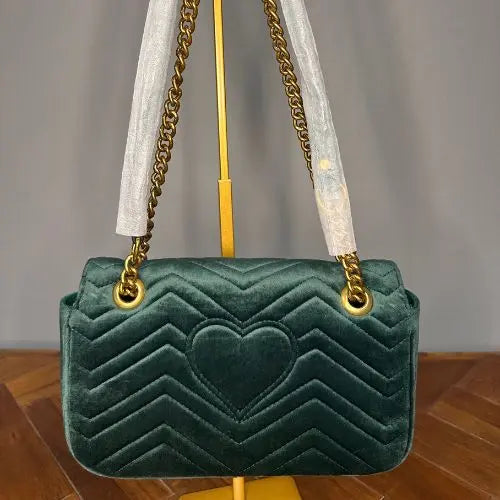 Green velvet handbag with gold chain strap showing the back with heart detail.