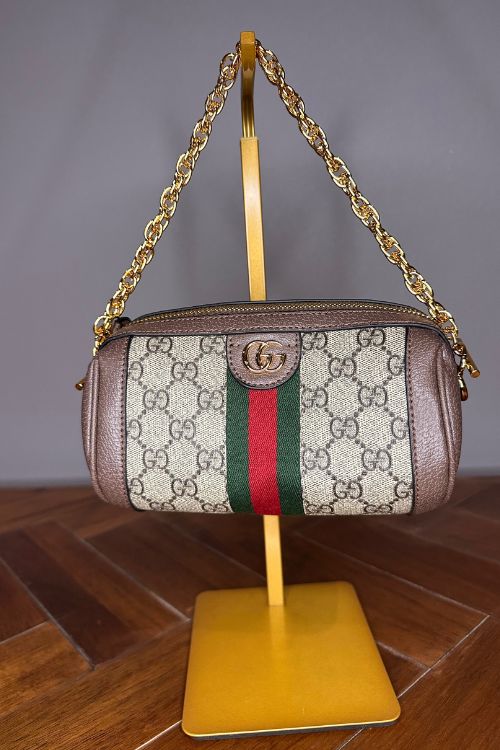 Designer handbag with chain strap on a stand against a neutral background