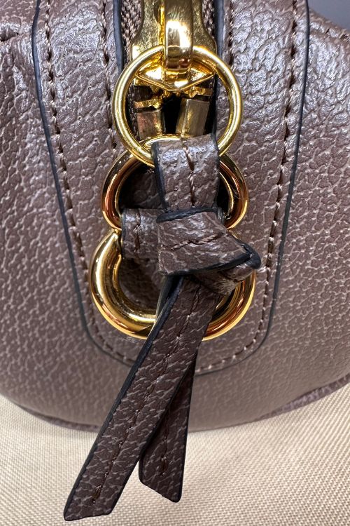 Close-up of a brown leather handbag with gold hardware and a strap.