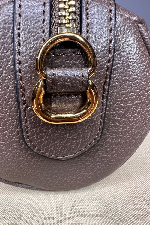 Close-up of a brown leather handbag with a gold buckle on a neutral background