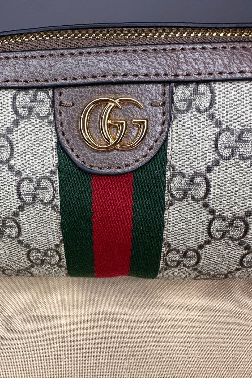 Gucci handbag with GG pattern and iconic green and red stripe on a beige surface