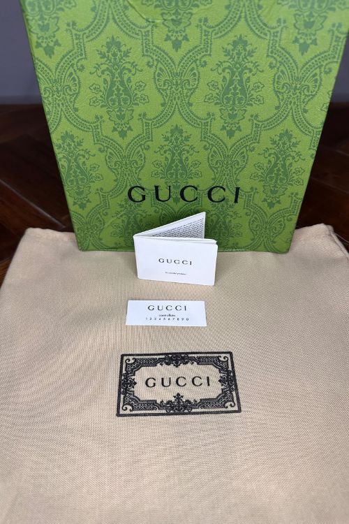 Gucci branded items including a green box, card, and card holder on a beige surface.