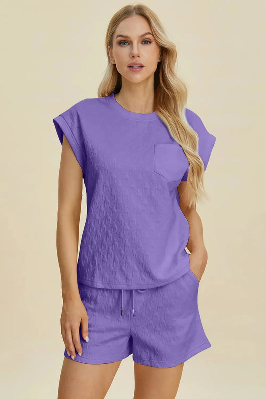 Ease meets elegance in this textured two-piece lounge set, featuring a short-sleeve top with a round neckline and functional chest pocket. The matching shorts are designed with an elastic waistband and side pockets, offering unrestricted comfort without compromising style. The soft lavender hue adds a refreshing pop to your off-duty look—perfect for warm days, staycations, or casual brunches. Whether worn as a set or styled separately, this duo brings versatility to your everyday edit.
