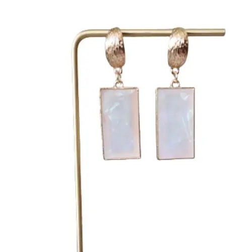 Rectangular white iridescent drop earrings with gold hoops displayed on jewelry stand — modern boutique accessories by Atlas by J&D.
