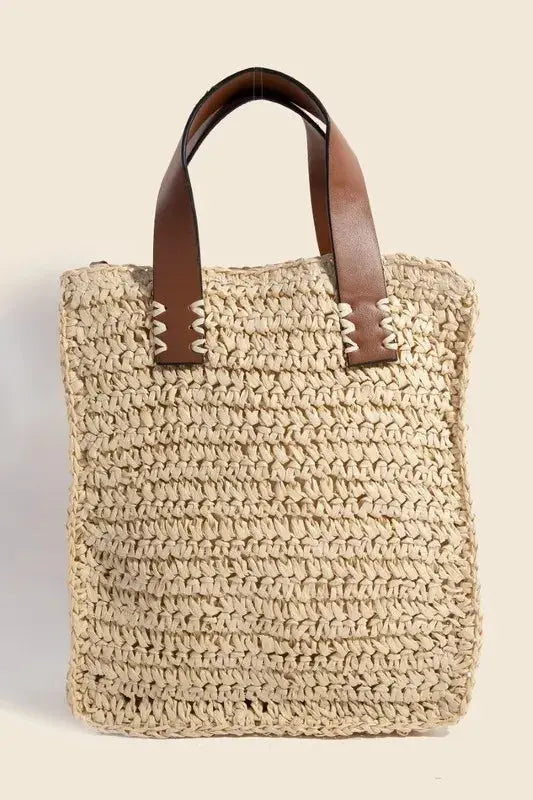 Woven straw bag with brown leather handles on a beige background.