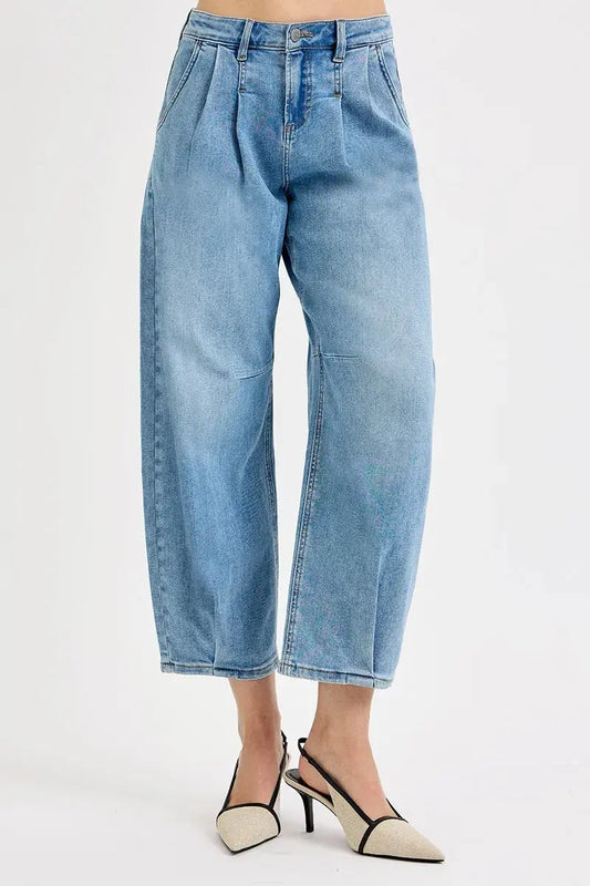 A person wearing light blue, cropped barrel jeans with a tan background.