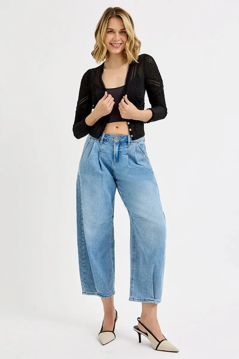 Woman wearing a black cropped jacket and light blue barrel style jeans on a white background.