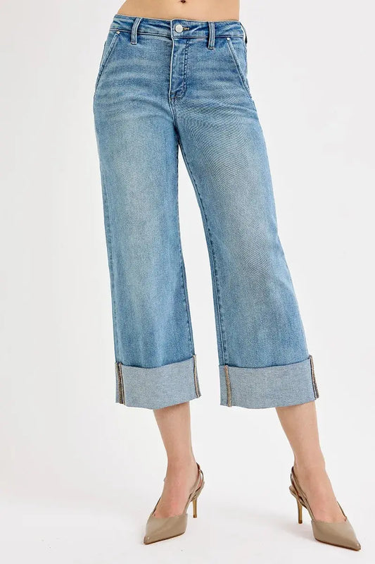Blue jeans with rolled-up cuffs worn by a person on a white background
