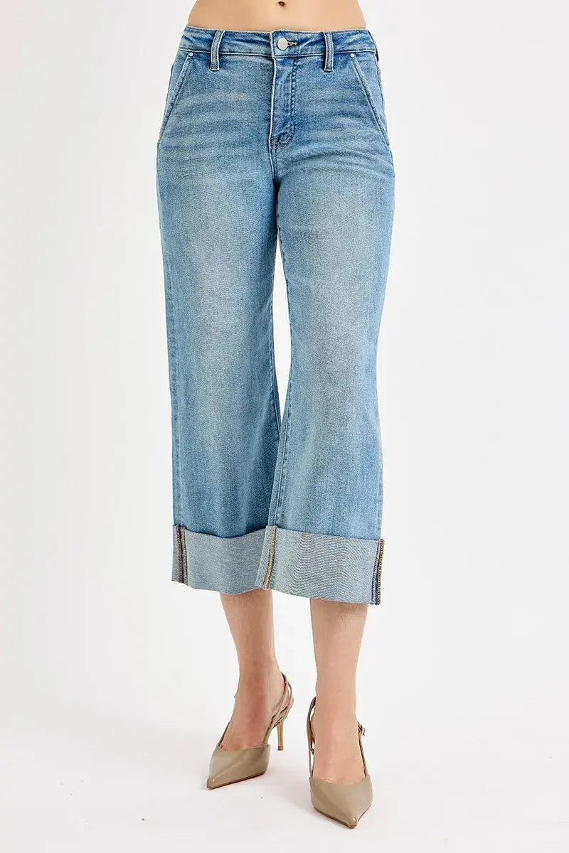A person wearing light wash jeans with rolled-up cuffs on a white background