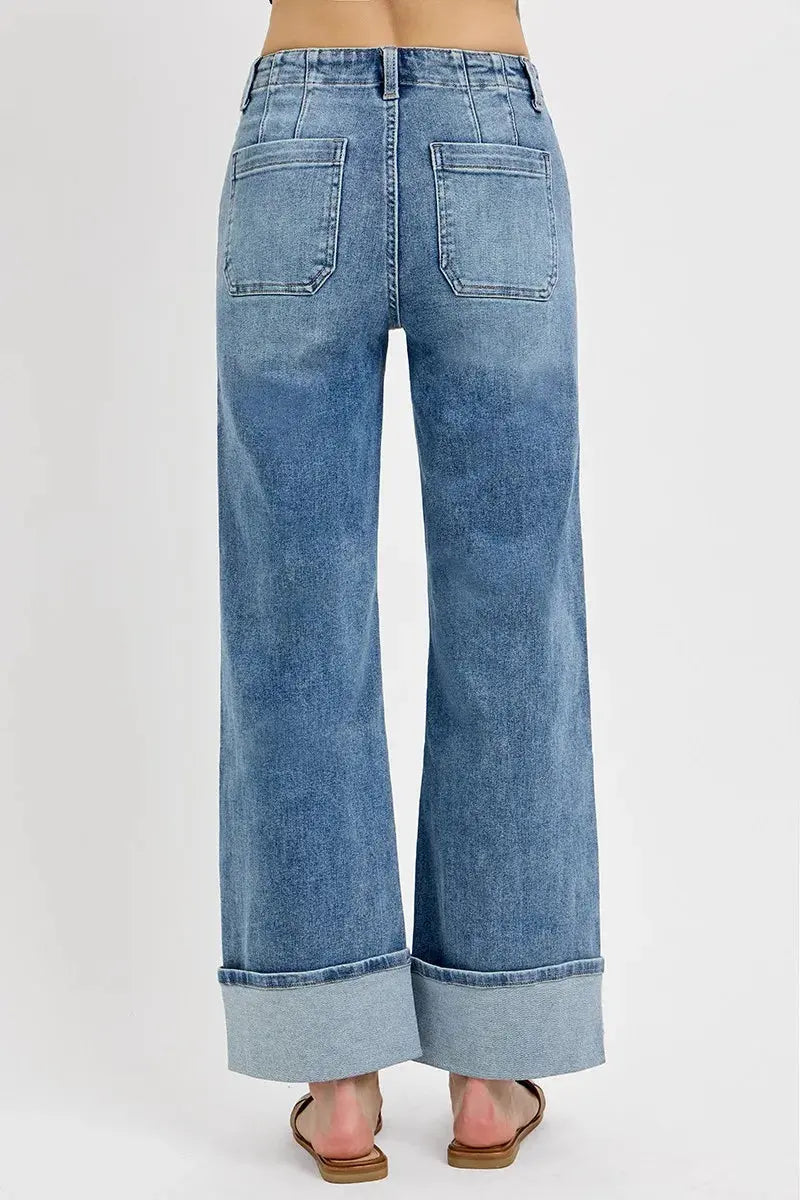 The back of wide leg blue jeans with a rolled hem on a white background