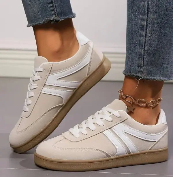 Beige sneakers with white stripes worn with blue jeans on a neutral background.