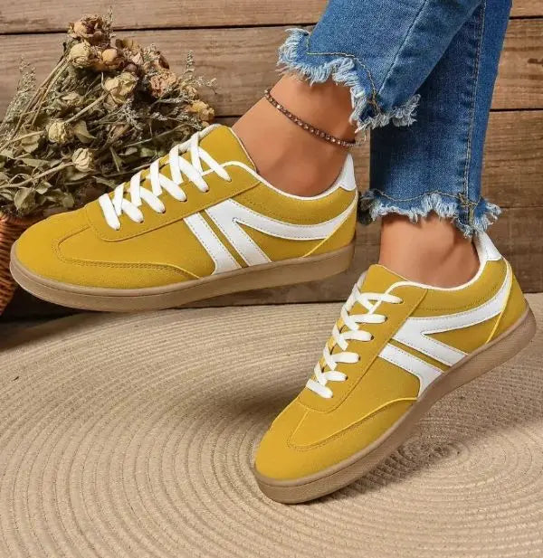 Yellow sneakers with white stripes worn by a person on a wooden floor.