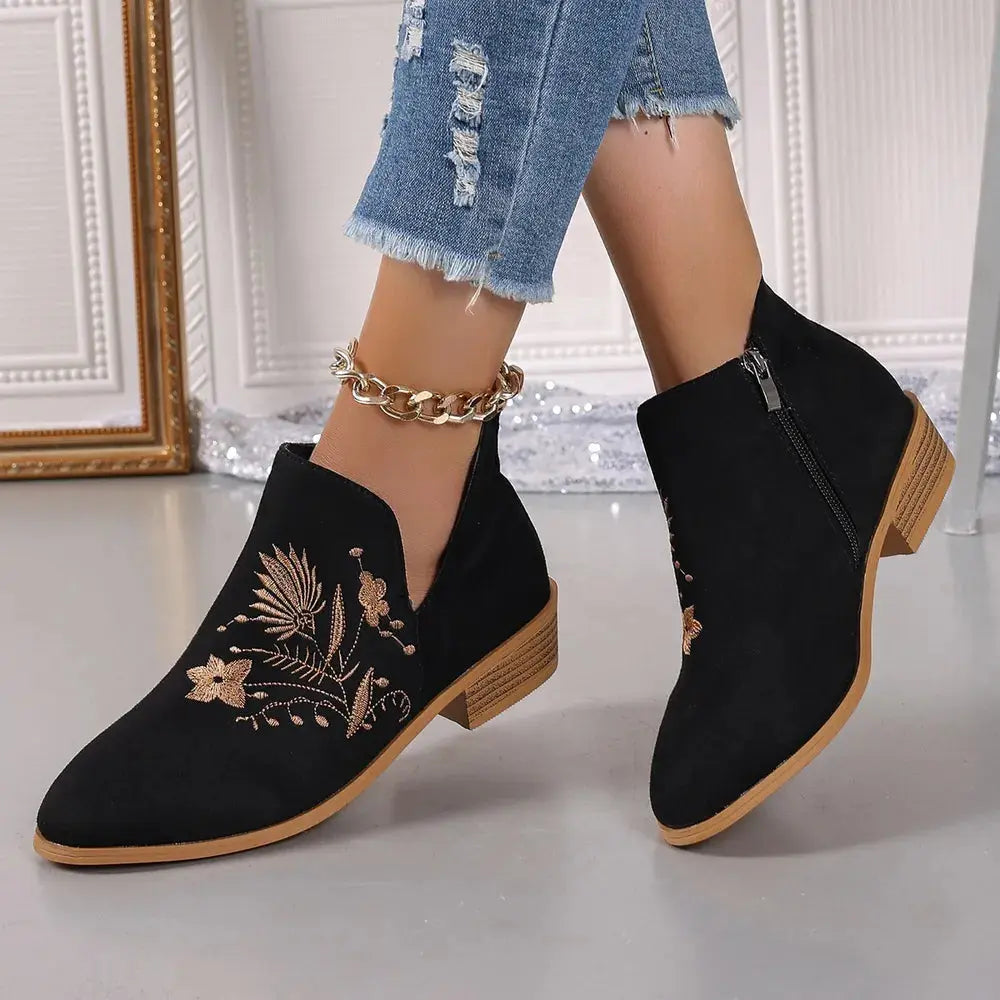 Black ankle boots with floral embroidery worn with blue jeans and a gold anklet.