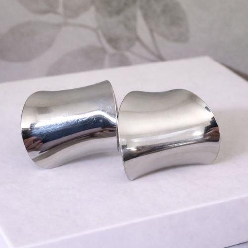 Two silver cuff earrings on a white box with floral background
