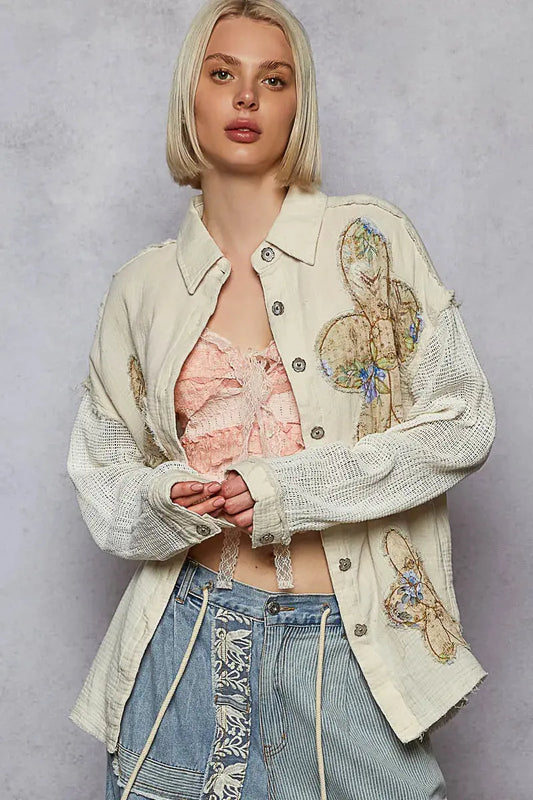 Woman wearing a stylish jacket with floral embroidery and crocheted sleeves on a gray background.