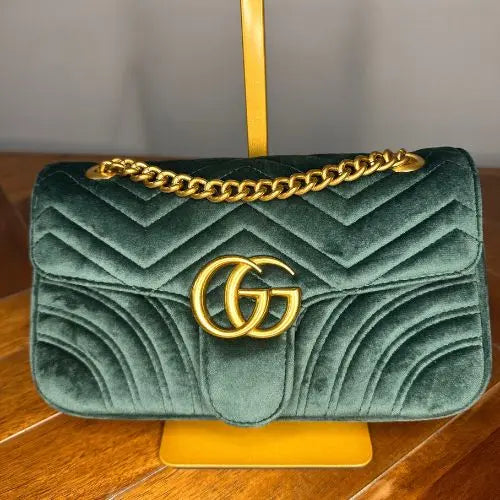 Green quilted handbag with gold chain and logo on a wooden surface