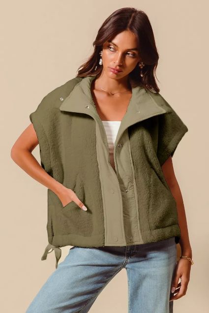 Woman wearing an olive green oversized zip front sherpa vest styled with light wash denim. Sleeveless streetwear inspired top with a wide collar and relaxed fit.