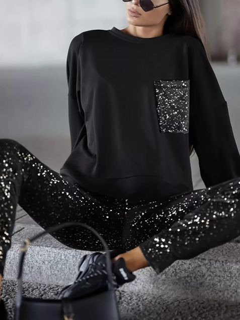 Model wearing black glitter pocket top with matching joggers in a relaxed seated pose showcasing the shimmer finish.