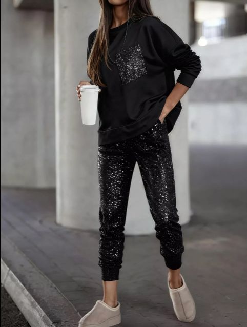 Model wearing a black long sleeve top with a glitter pocket and matching black joggers with glitter detail styled for a casual elevated look.