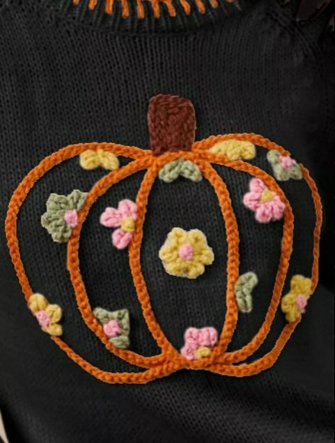 Detailed close-up of the pumpkin embroidery on a black knit sweater, showcasing multicolor floral stitching and warm seasonal tones.