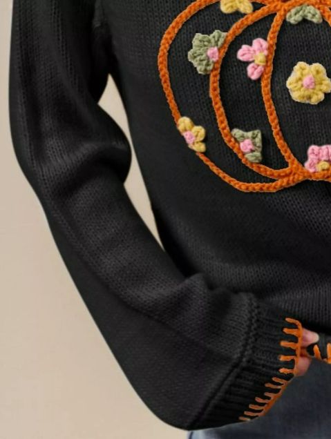 Black knit pumpkin sweater shown from the side, highlighting relaxed sleeve movement and orange trim along the hem and cuffs.